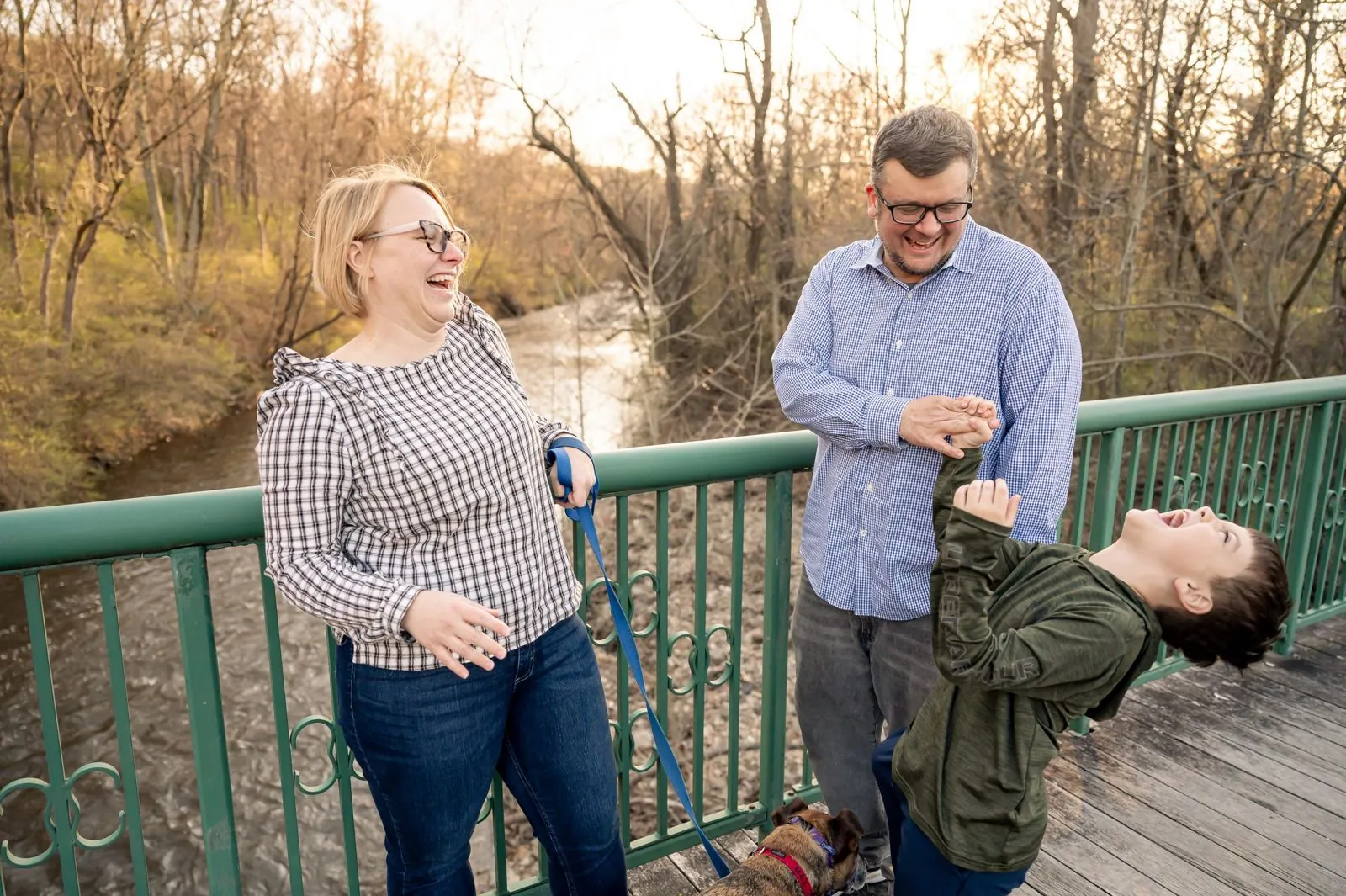 A mom, a dad and their son laughing on a footbridge